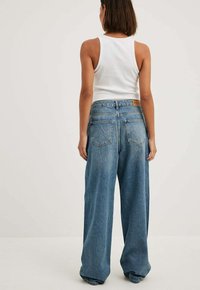 Aukštai juosmeninės, plačios kojelės mėlynos džinsinės kelnės su blukintu paviršiumi, su dviem užpakalinėmis kišenėmis ir odiniu logotipo ženkleliu ant juosmens.