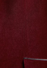 Burgundi színű szövet, puha, bolyhos textúrával, látható varrással és egy vékony fekete akcentussal az alsó szélén.