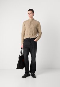 Camisa de lino beige con cuello mao y botones, combinada con jeans gris oscuro y zapatos negros, sosteniendo una bolsa tote negra.