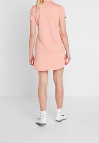 Šaty s krátkým rukávem a límečkem v světle růžové látce. Mají rozšířenou sukni a boční rozparek, doplněné bílými sportovními botami a ponožkami.