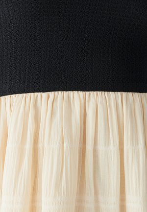 Bodice supérieur noir texturé avec une partie inférieure beige clair froncée ; tissu doux et fluide avec un effet superposé.