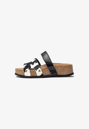 Claquette en cuir noir et blanc à imprimé vache avec un pied en liège, équipée de deux brides avant et d'une bride en cuir noir moulé pour un soutien.