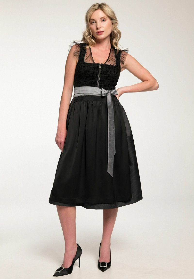 Schwarzes Kleid mit strukturiertem Oberteil,transparenten gepunkteten Trägern und einem plissierten Rock. Mit einem grauen Gürtel in der Taille und schwarzen High Heels.