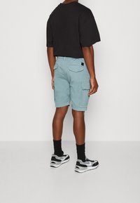 Cargo shorts i ljusblått tyg med sidfickor och en bakficka, kombinerade med en svart oversized t-shirt och svarta strumpor, kompletterat med sneakers.