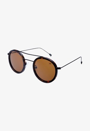 Lunettes de soleil rondes avec une monture en écaille de tortue, des verres marron et des branches noires fines en métal. Présentent un double pont et des plaquettes de nez transparentes.