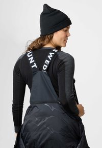 Zwarte beanie, grijs longsleeve shirt met versterkte schouders en een zwarte zipvest met verstelbare banden met de opdruk "SWED".