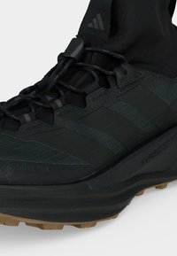 Μαύρο πεζοπορικό παπούτσι Adidas με υλικό Gore-Tex, χοντρή υφή στη σόλα και μαύρα κορδόνια, εμφανίζει τις ρίγες της Adidas και τη μεσαία σόλα Hyperboost.