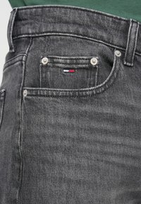 Σκούρο γκρι τζιν με λεπτή εφαρμογή, διαθέτει μπροστινή τσέπη με ασημένια μεταλλικά στοιχεία και μικρή τρισχρωμία λογότυπο κοντά στην τσέπη.