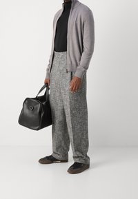Cardigan grigio lavorato a maglia sopra un dolcevita nero, abbinato a pantaloni grigi chiari con texture e borsa a sacco in pelle nera. Sneakers nere con dettagli marroni.