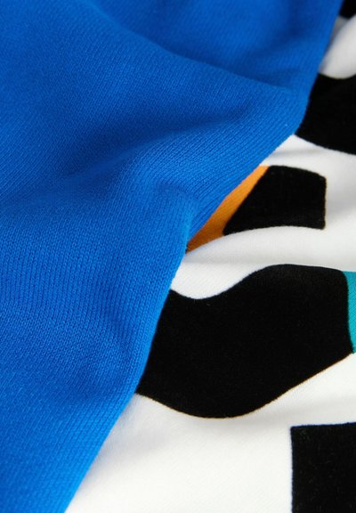 Primer plano de tela azul texturizada sobre un paño blanco con formas abstractas en negro, naranja y verde azulado.