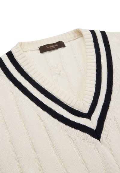 Maglione crema lavorato a maglia con scollo a V, caratterizzato da dettagli a strisce nere e bianche sul colletto e una texture a trecce su tutta la superficie.