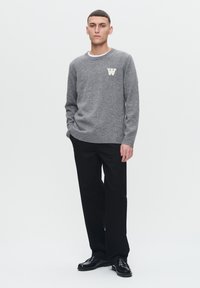 Gray knit sweater with a round neck, featuring a cream letter "W" on the chest. Paired with black straight-leg trousers and black shoes.