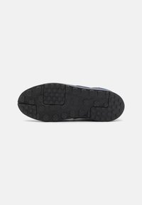 Black rubber shoe sole with circular and hexagonal traction patterns, sturdy construction, and contrasting dark blue upper fabric.