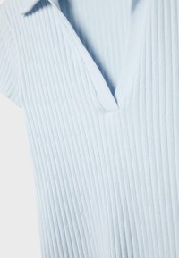 Svetlomodrá rebrovaná látka s hlbokým výstrihom do V a krátkymi rukávmi, prezentujúca textúru a detaily goliera odevu.