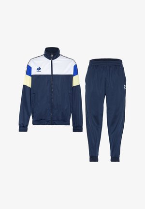 Marineblaue Trainingsjacke mit weißen, blauen und gelben Farbfeldern, kombiniert mit marineblauen Trainingshosen mit elastischem Bund und Reißverschluss vorne.