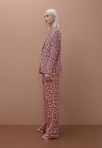 Blazer de estampado de leopardo y pantalones a juego en tonos de rosa, naranja y púrpura, con una textura suave y tacones metálicos abiertos en los dedos.