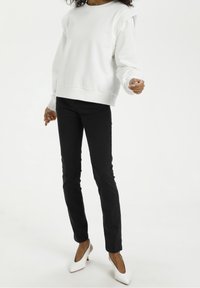 White sweatshirt with dropped shoulders, ribbed cuffs, and hem. Paired with black skinny jeans and white heels. Simple, modern design.