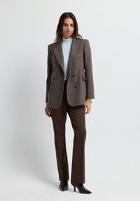 Blazer doppiopetto marrone a motivo Houndstooth con rever a scialle, abbinato a un dolcevita blu chiaro e pantaloni sartoriali marroni. Tacchi a punta neri.