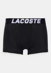 Boxeri negri dintr-un material neted, prevăzuți cu un brâu elastic lat pe care scrie "LACOSTE" în alb și un logo discret pe lateral.