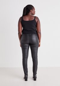 Black tank top and fitted faux leather pants, featuring a smooth texture, back pockets, and a tapered leg design with zippers at the ankles.