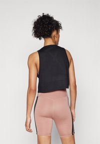 Czarny krótki top na ramiączkach z szerokimi otworami na ramiona, zestawiony z różowymi szortami z czarnymi paskami po bokach, prezentującymi gładką, dopasowaną fakturę.