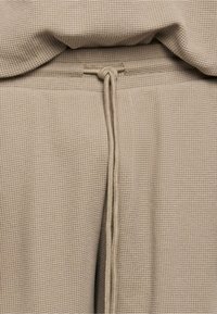 Gros plan sur un tissu beige en maille gaufrée avec une capuche et un cordon noué au centre.