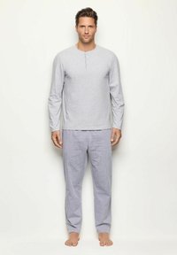 Camisa henley de manga larga gris con un tapón de tres botones, combinada con pantalones de pijama a rayas azul claro. Tejido suave con un corte relajado.