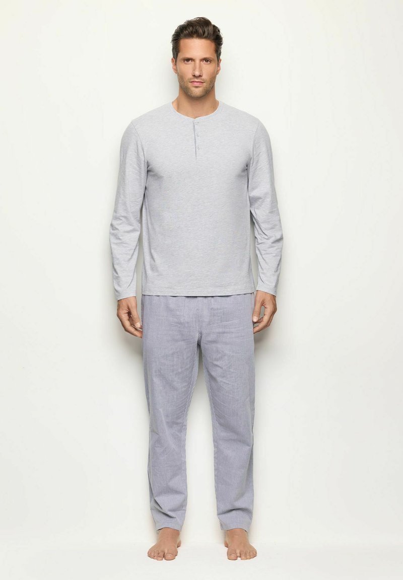 Camisa henley de manga larga gris con un tapón de tres botones, combinada con pantalones de pijama a rayas azul claro. Tejido suave con un corte relajado.