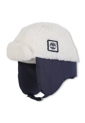 Chapeau d'hiver doublé en polaire avec une couche extérieure blanche, des côtés bleu marine, une sangle sous le menton et un écusson avec logo. Texture douce avec une forme arrondie.