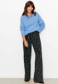 Pull bleu clair duveteux à manches longues, associé à un pantalon noir avec un motif en zigzag et des accents scintillants, porté avec des chaussures noires.