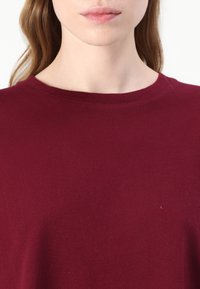 Bordó krátký rukáv bavlněný top s kulatým výstřihem a hladkou, jemnou texturou. Jednoduchý design bez viditelných vzorů nebo akcentů.