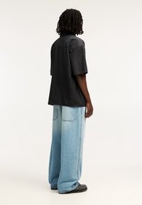 Camicia nera a maniche corte con vestibilità rilassata, abbinata a jeans denim a gamba larga di colore azzurro chiaro, con tasche posteriori e finitura sbiadita.