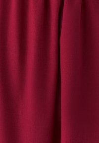 Tela burdeos con superficie texturizada y tejida, que presenta caídas suaves y un brillo sutil, adecuada para ropa o tapicería.