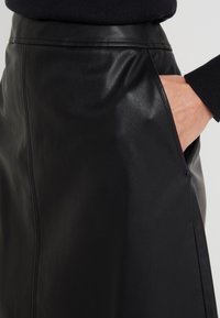 Musta nahkahame, jossa on sileä pinta, sivutasku ja hienovaraiset ompeleet vyötäröllä. Malli on virtaviivainen ja vartalonmyötäinen.