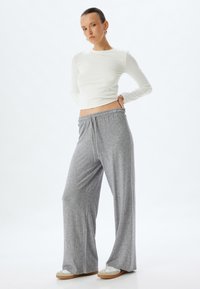 Leichtes, eng anliegendes, weißes Langarmoberteil kombiniert mit lockeren, grauen Sweatpants mit elastischem Bund und Kordelzug.