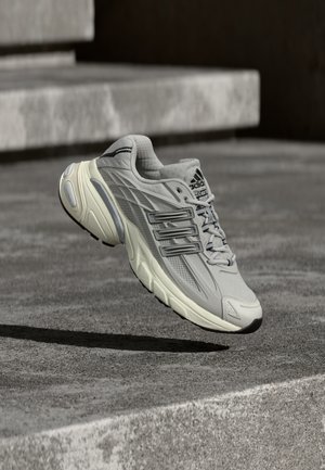 Chaussure de course Adidas gris clair avec semelle amortissante flottant au-dessus d'escaliers en béton en extérieur.