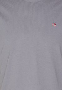 Lysegrå t-skjorte laget av glatt stoff, med et lite brodert rødt og hvitt norsk flagg på brystet.