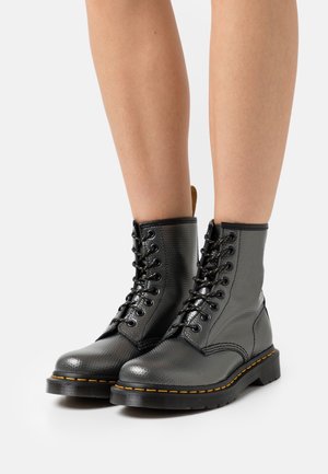 Svarta läderstövletter med strukturerad yta, rund tå och gul söm. Har snörning högt upp och robust sula.