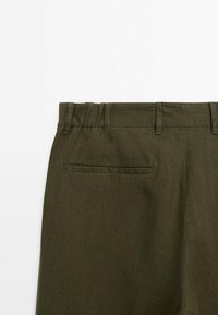 Pantaloni in lino verde oliva con vita piatta, passanti per cintura e due tasche posteriori. Texture liscia e vestibilità sartoriale.