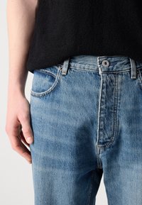 Világoskék farmernadrág, egyenes szabással, öt zsebes dizájnnal és látható varrási részletekkel. Fekete top mellett viselve.