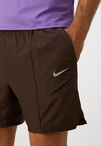 Bruna sportshorts i lättviktig textil, med en sidficka som har en stilren silverfärgad Nike-logotyp och en liten sidoöppning för ökad rörlighet.