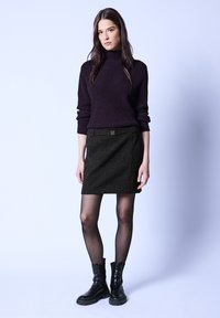 Tmavě fialový pletený rolák spárovaný s černou sukní s detaily pásku. Černé kotníkové boty a průhledné černé punčocháče dotvářejí vzhled.