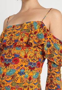 Top con hombros al descubierto que presenta un vibrante patrón floral en tonos naranja, azul, rojo y verde. Diseñado con acentos de volantes y tirantes delgados.