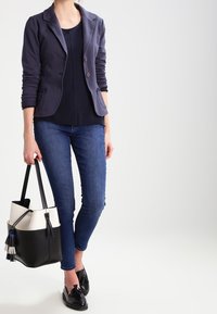 Námořnický blejzr se dvěma knoflíky a předními kapsami, v kombinaci s tmavým tričkem, úzkými džíny a černými mokasíny; nosí černobílou kabelku.