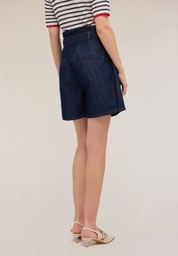 Pantalones cortos de mezclilla en azul oscuro con una cintura alta ajustable, que cuentan con dos bolsillos traseros y un corte recto. Textura suave y dobladillo limpio.