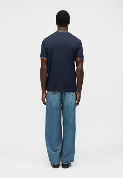 Μπλε-ναυτικό μπλουζάκι με στρογγυλή λαιμόκοψη, κοντά μανίκια και αντίθετη λεπτομέρεια, συνδυασμένο με μπλε τζιν παντελόνι φαρδιάς γραμμής. Λείο ύφασμα, άνετη εφαρμογή.