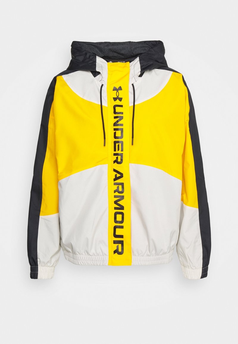 Kurtka z kapturem z żółtymi, białymi i czarnymi panelami kolorów, czarnymi sznurkami oraz logo i napisem „Under Armour” pionowo na froncie przy zamku błyskawicznym.