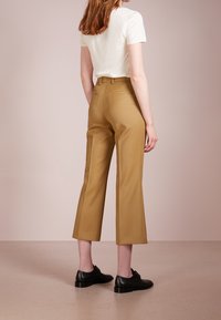 Ljusbeige åtsittande t-shirt i kombination med khaki capribyxor, med en mjuk textur, platta framfickor och svarta läderskor.