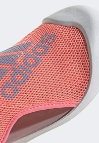 Scarpe sportive in rete rosa con logo blu, design aperto per traspirabilità, suola in gomma bianca e accenti dalla texture liscia.