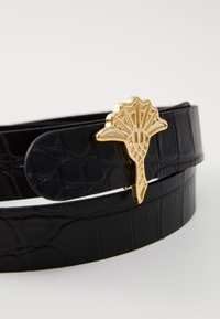 Cintura nera in ecopelle di coccodrillo con una fibbia decorativa dorata caratterizzata da un design a ventaglio. Doppia cinghia per una vestibilità regolabile.